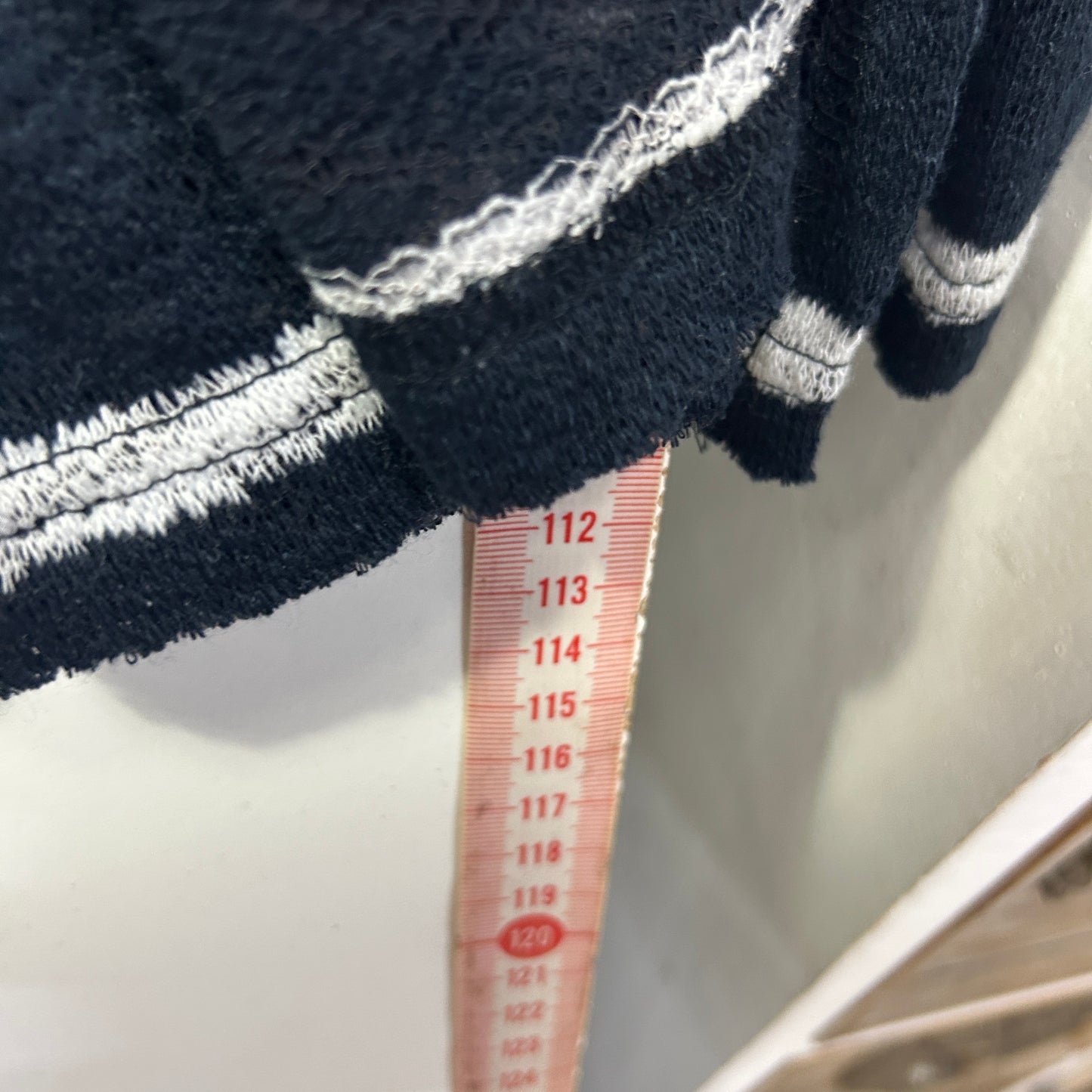 Black jumper detail view with white stripes and measurement ruler
