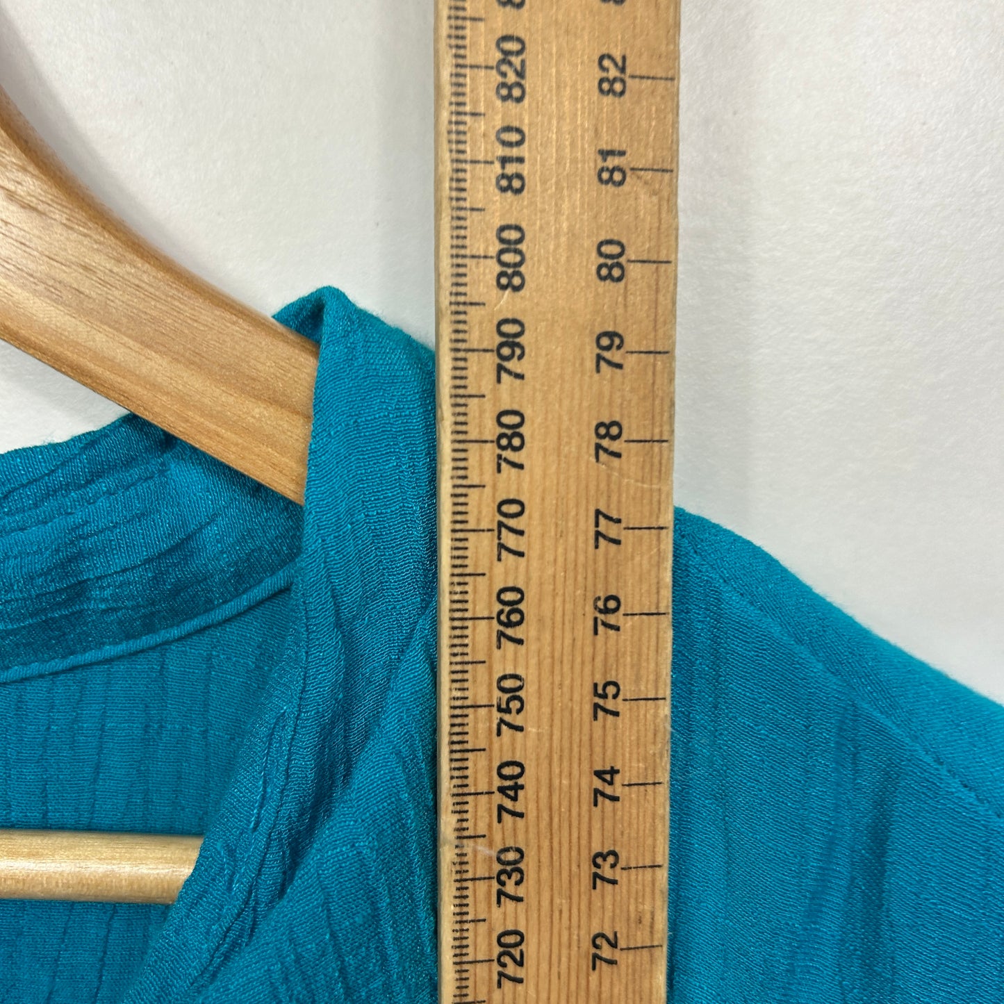 Teal garment detail view on wooden hanger with measurement ruler