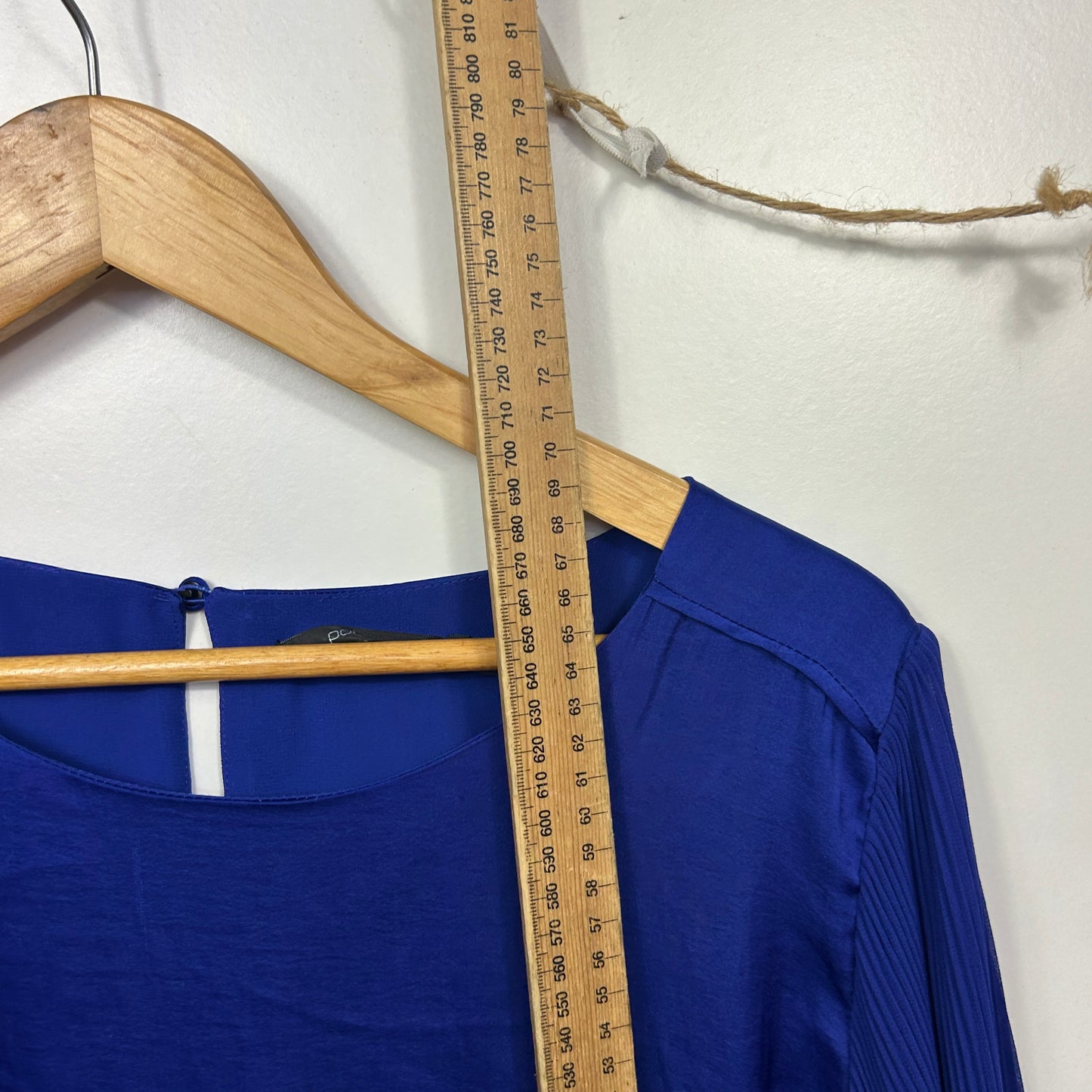 Blue long sleeve top front view on wooden hanger with measuring tape