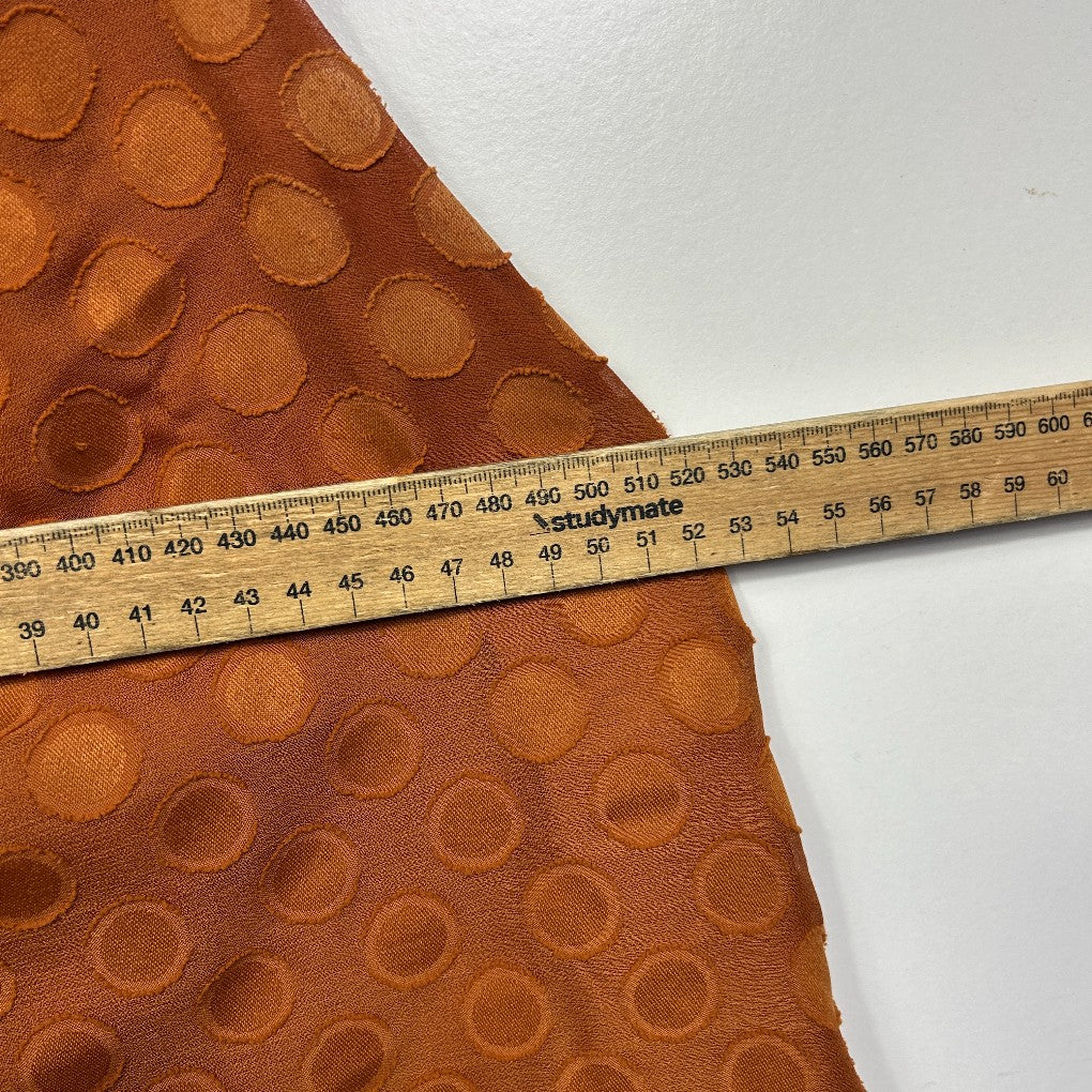 Rust orange textured fabric with circular embossed pattern detail view