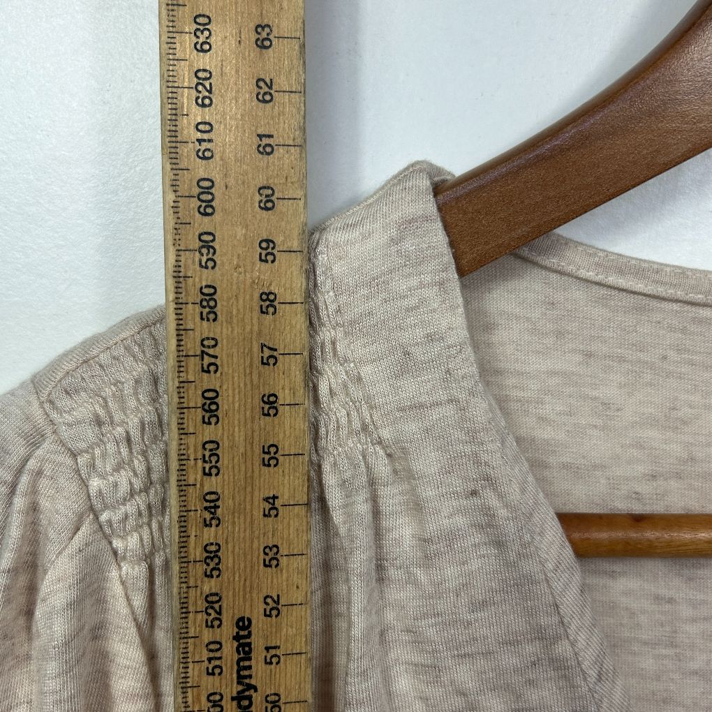 Beige linen shirt detail view with wooden hanger and measuring tape