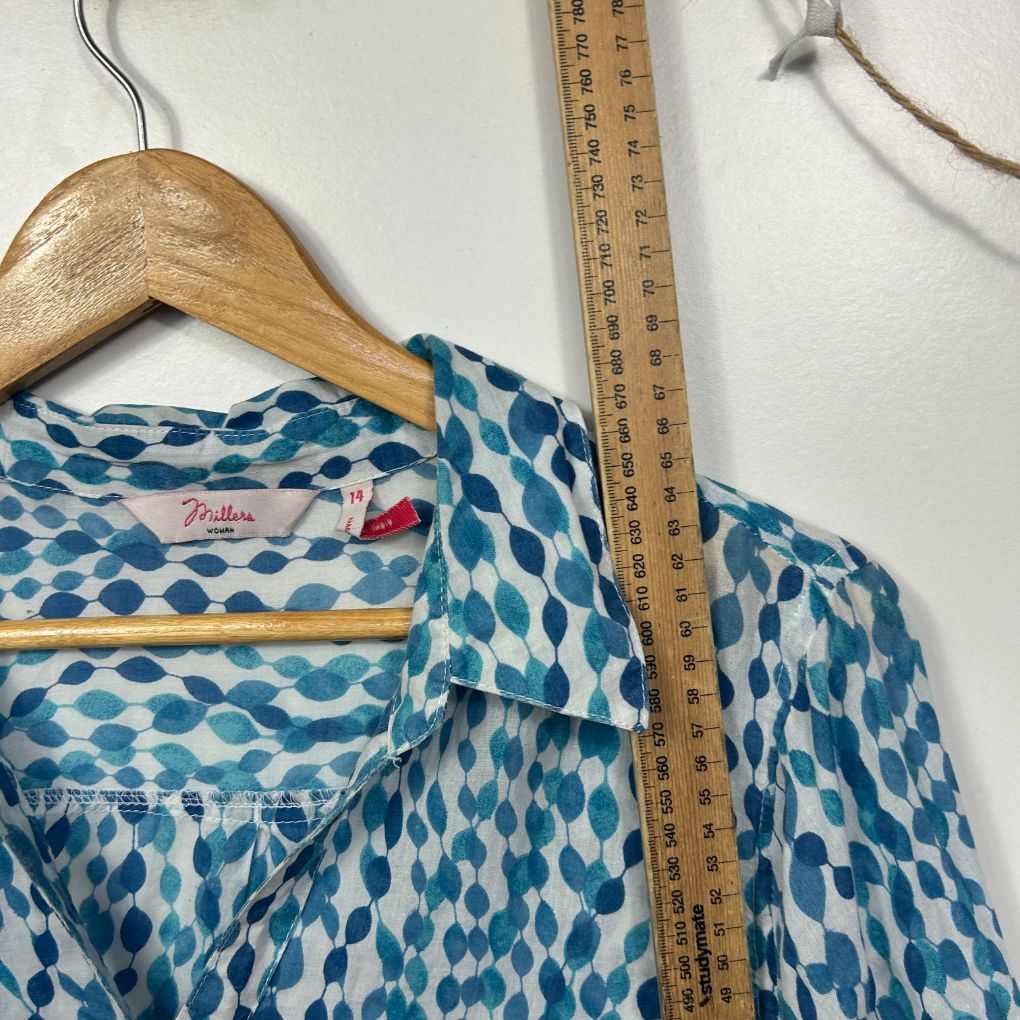 Blue and cream patterned blouse front view on hanger with measuring tape