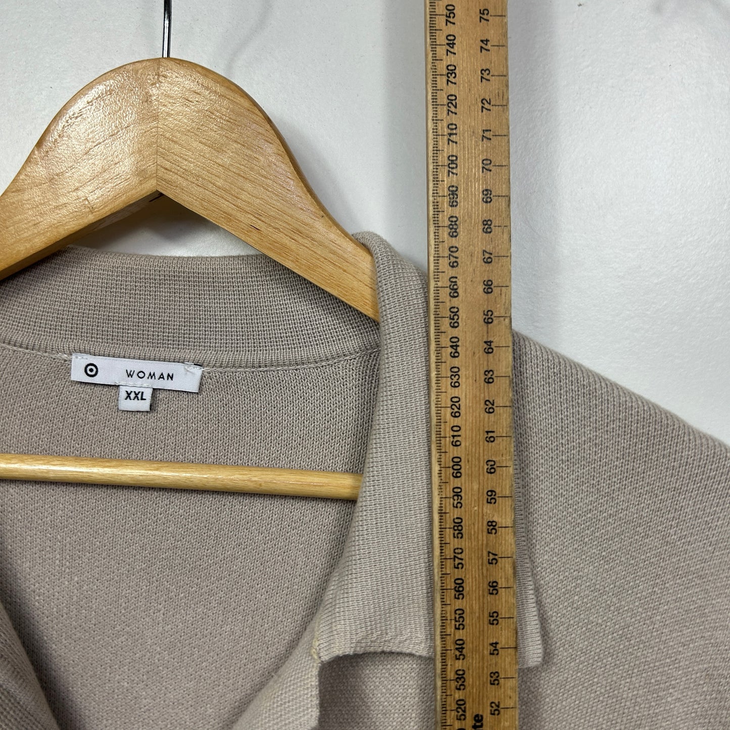Beige knit sweater front view on wooden hanger with measurement ruler