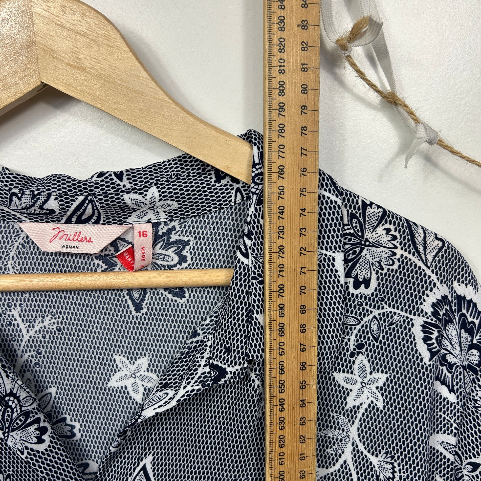 Black and white floral print top detail view on hanger with measuring ruler