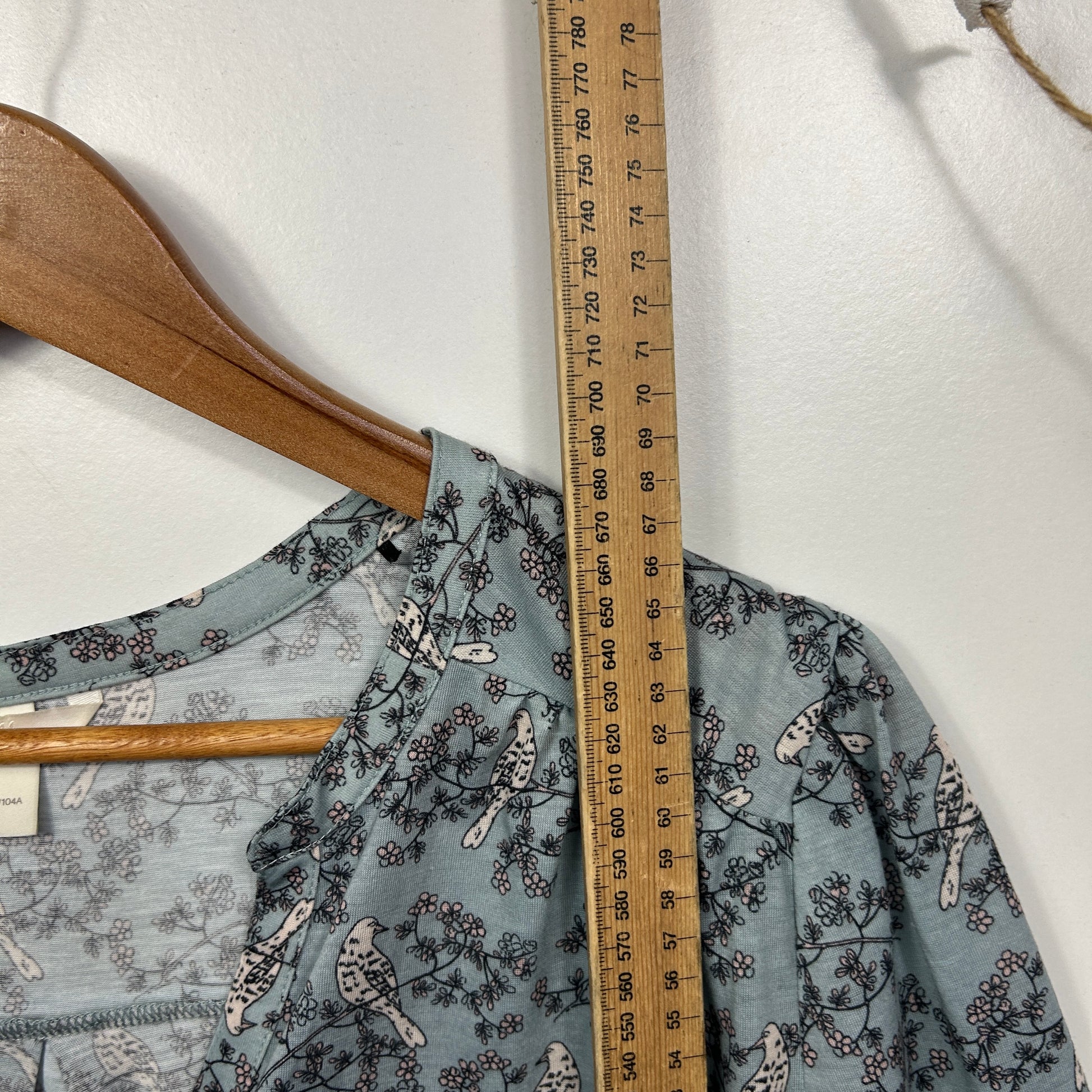 Grey floral blouse front view with wooden hanger and measuring tape
