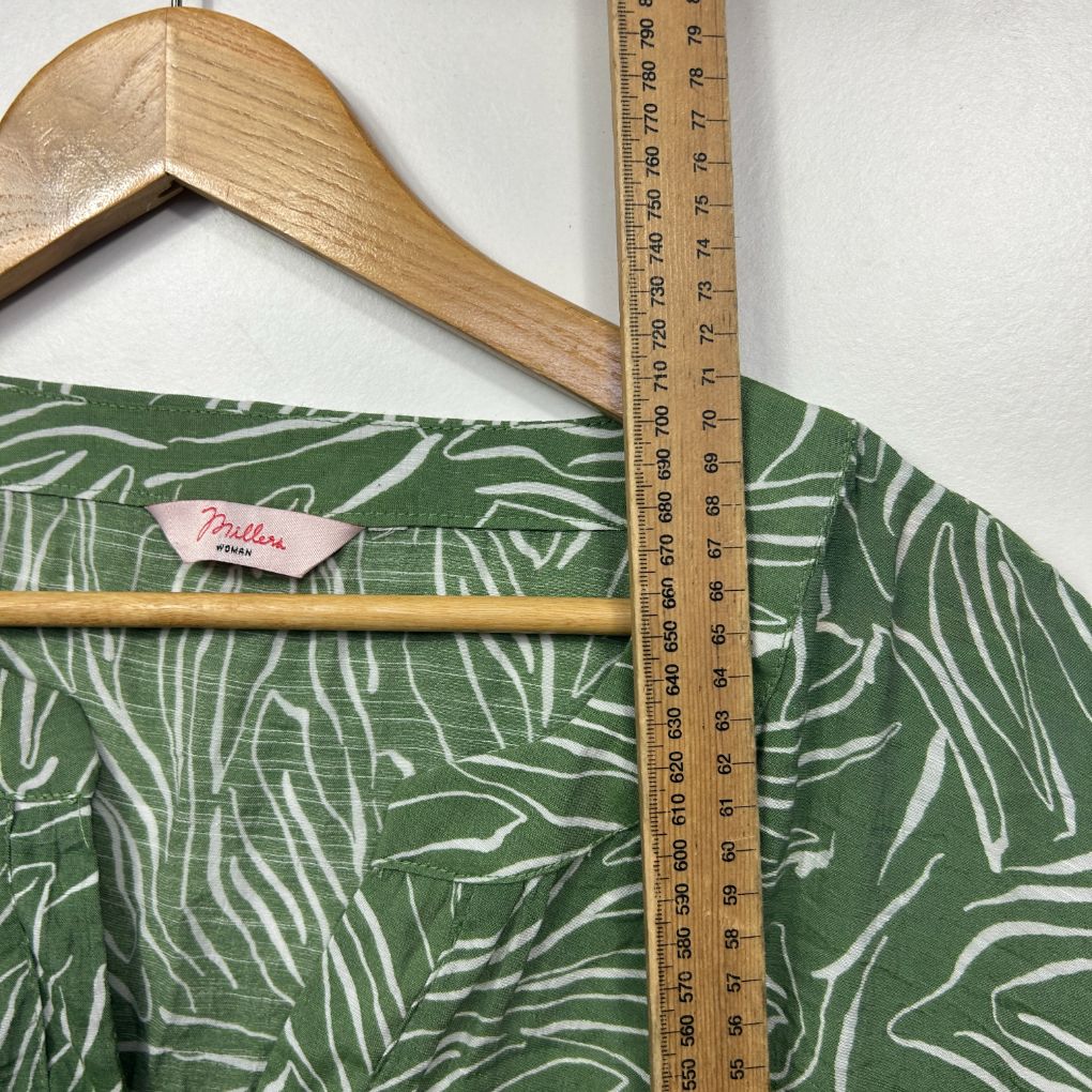 Green and white patterned shirt detail view on wooden hanger with measuring tape