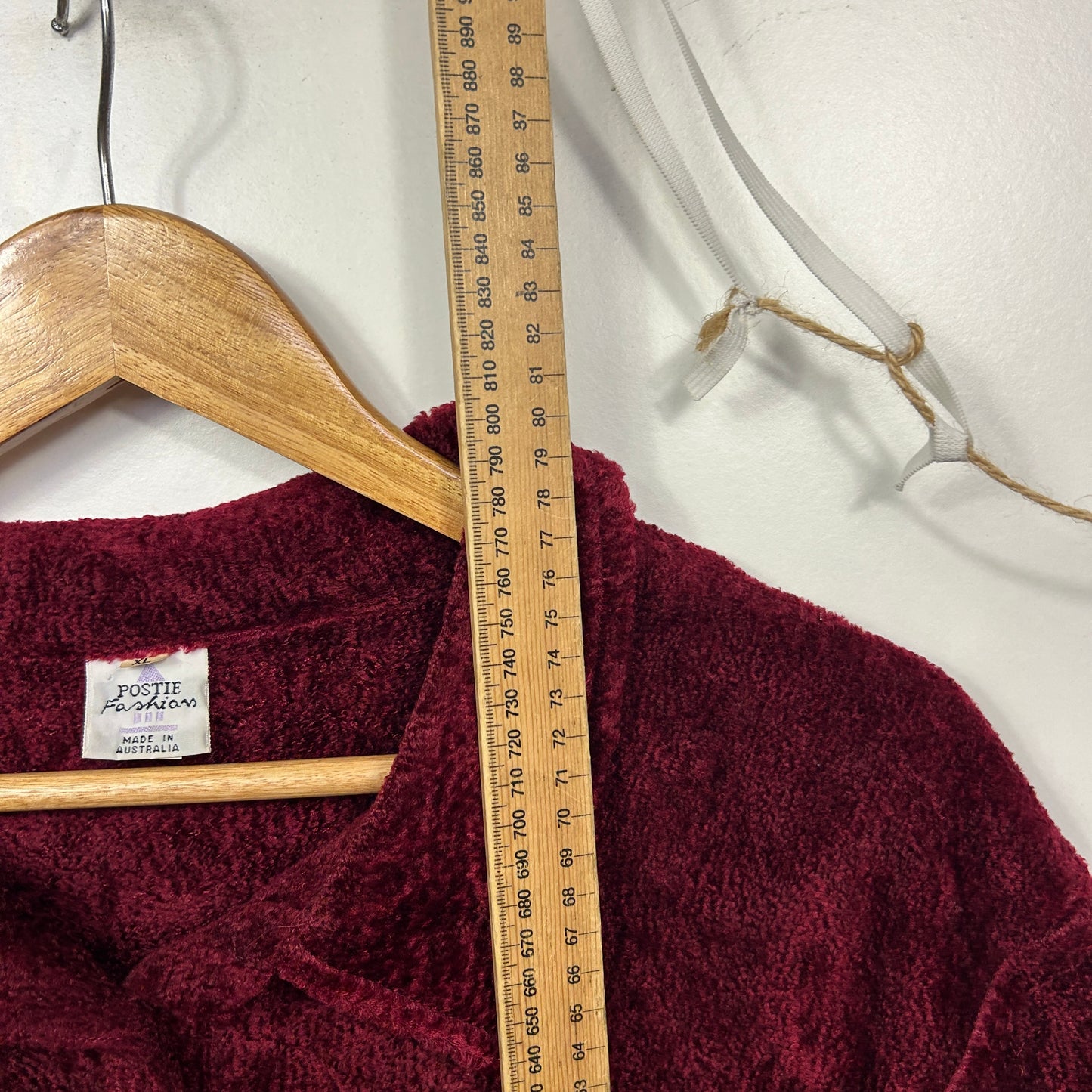 Burgundy jumper front view on wooden hanger with measuring tape