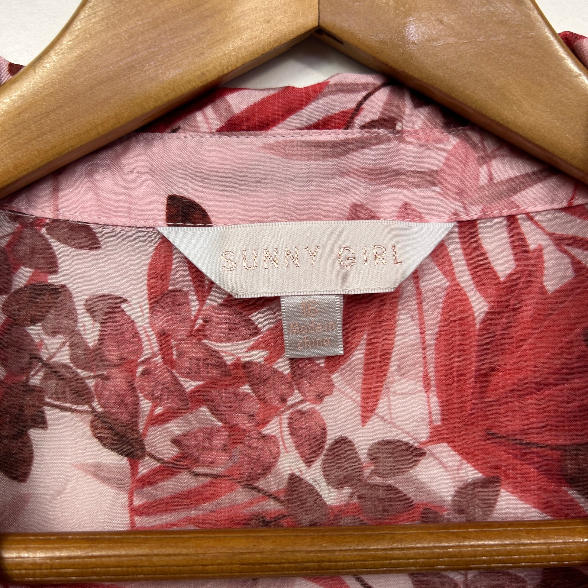 Pink floral shirt detail view on wooden hanger