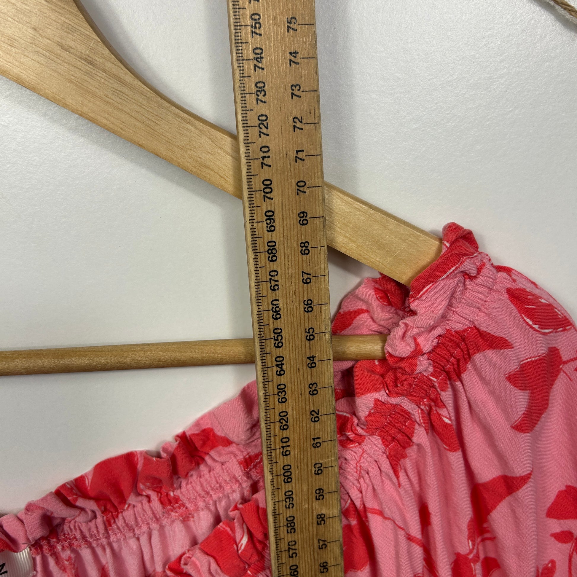 Red and pink patterned shorts detail view with elastic waistband and measuring ruler