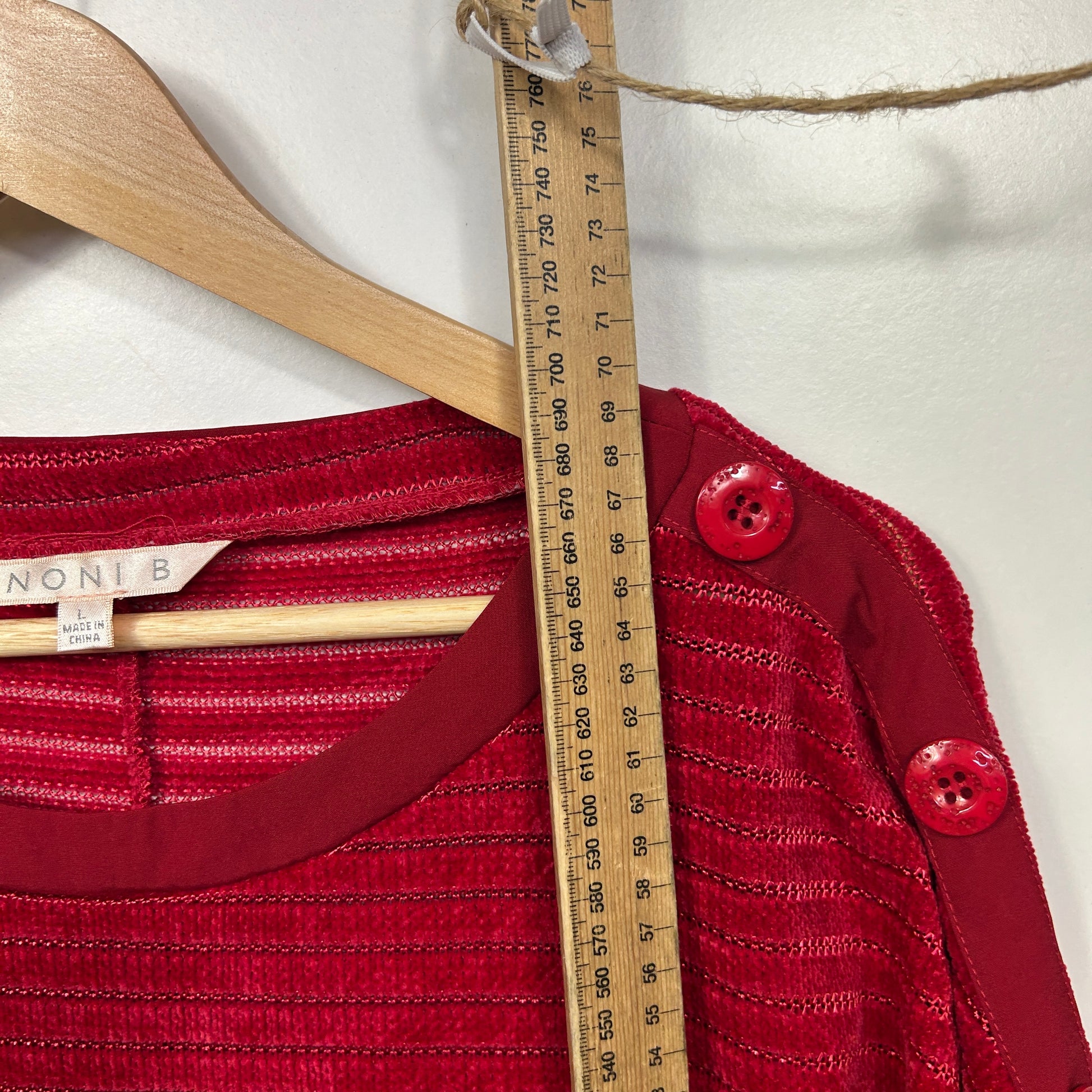 Red knit sweater detail view with wooden hanger and measuring tape