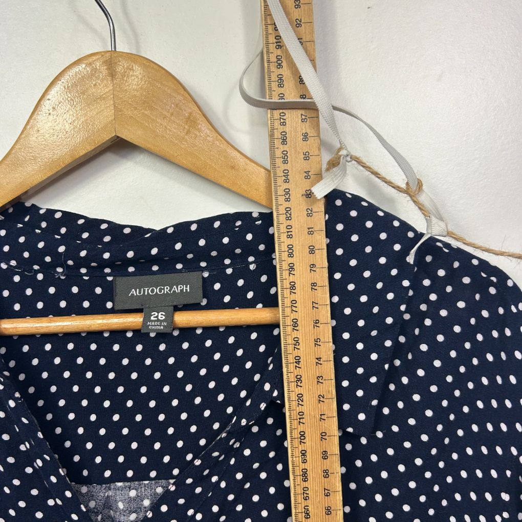 Navy polka dot top detail view on hanger with measuring tape