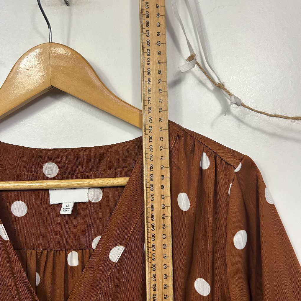 Brown polka dot blouse front view on wooden hanger with measuring tape