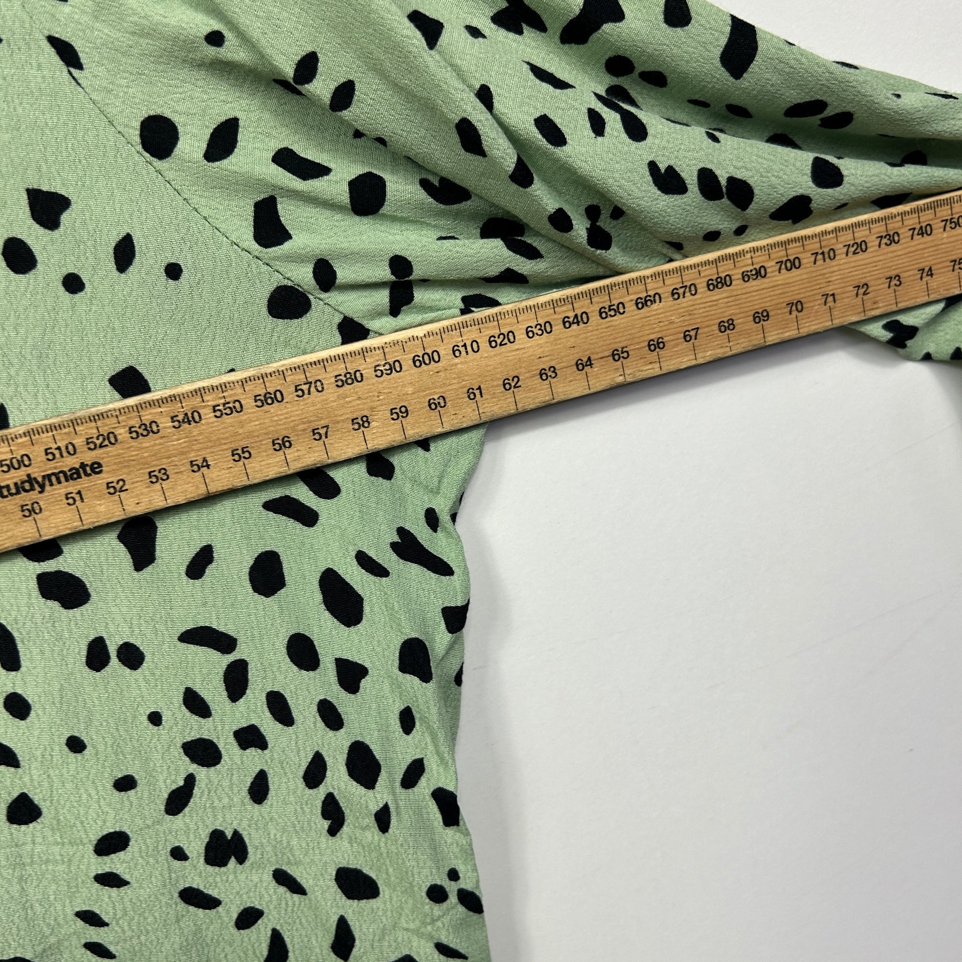 Sage green fabric with black speckled pattern and measuring tape detail view