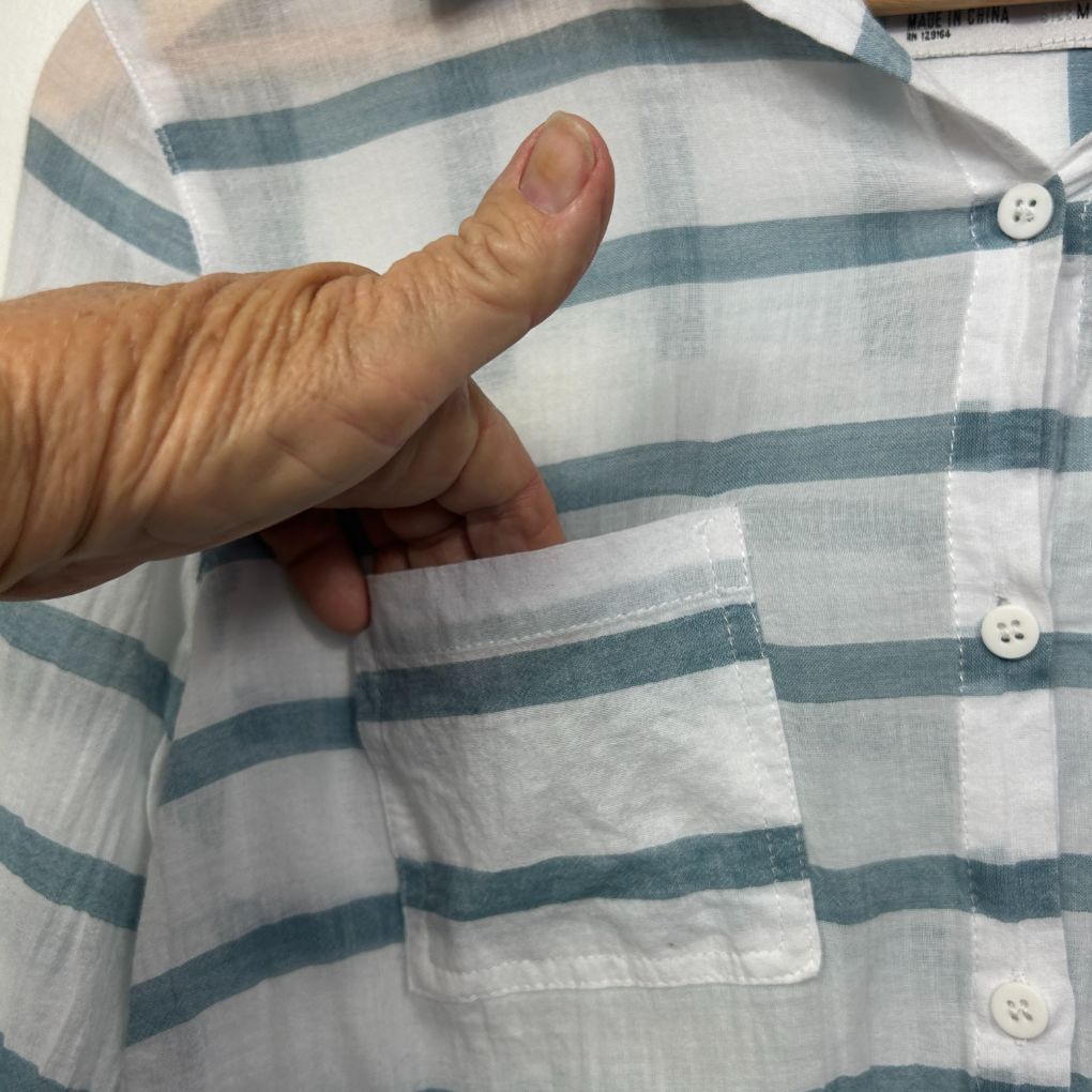 White and teal striped shirt front view with hand pointing to pocket detail