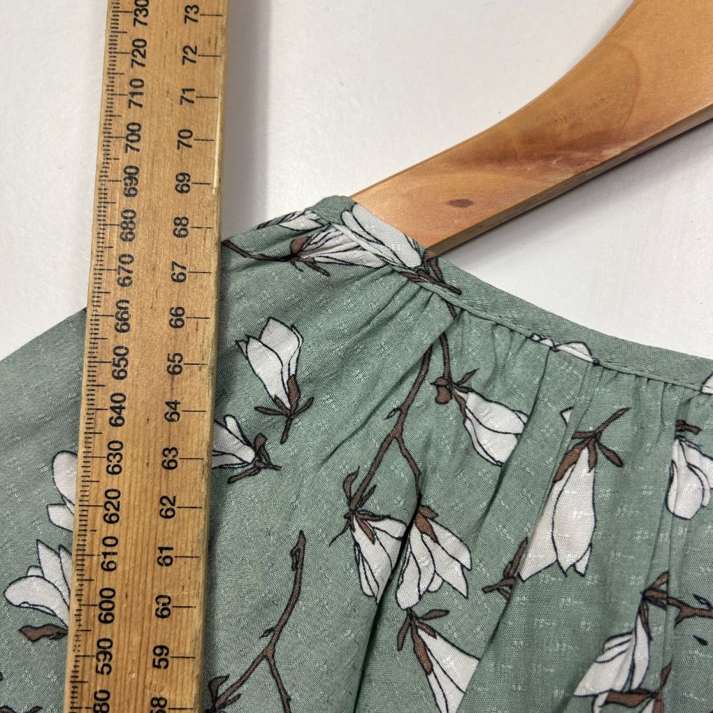 Sage green shirt with white and black floral pattern detail view with measuring tape