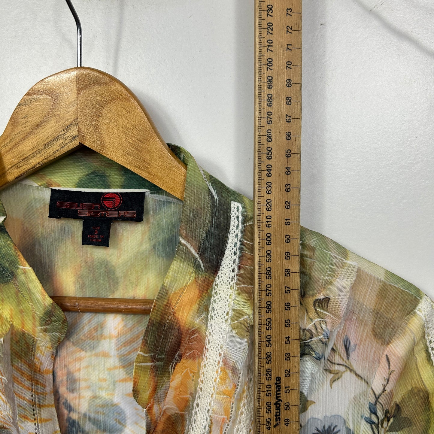 Green and yellow floral shirt front view on wooden hanger with measuring ruler