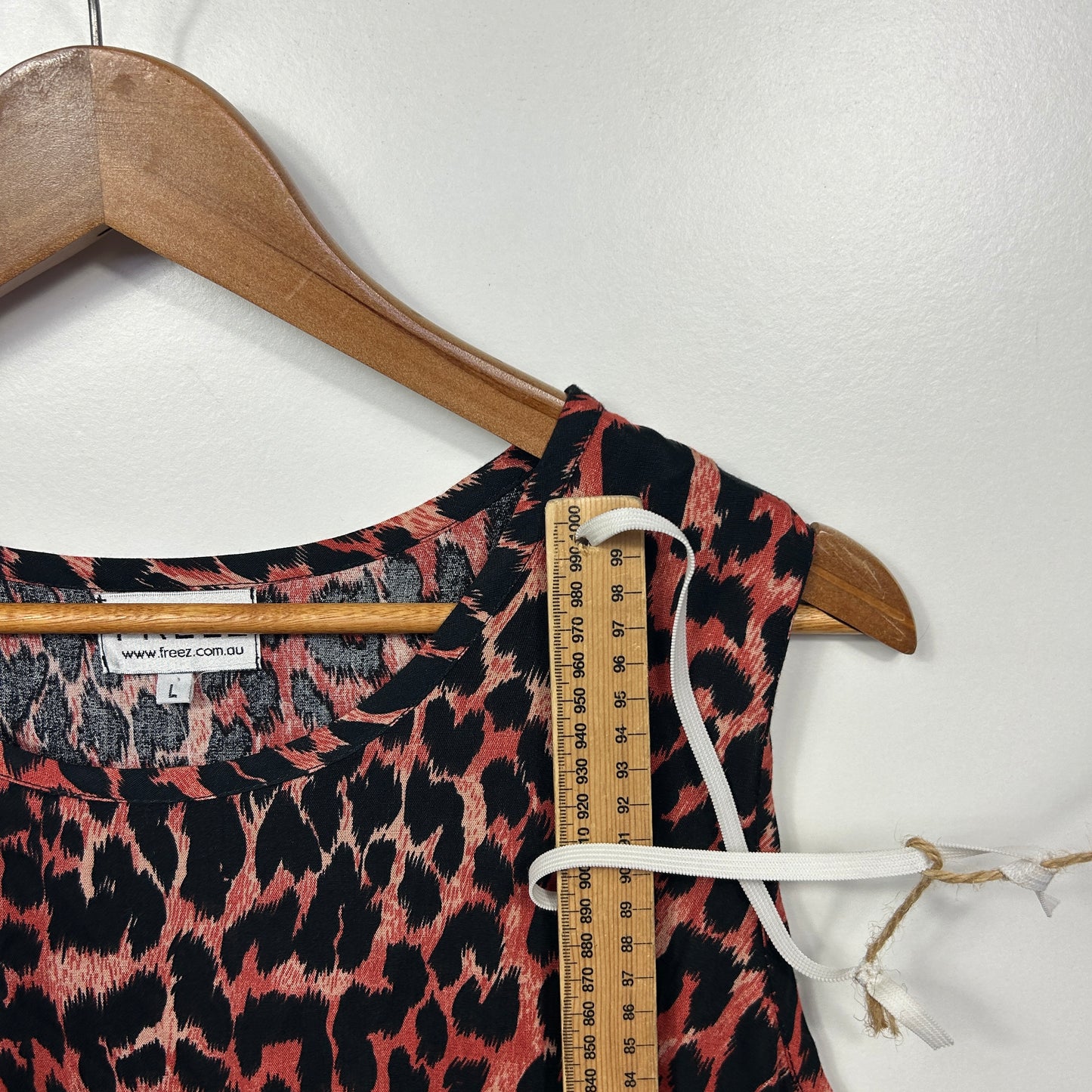 Red and black leopard print sleeveless top detail view on wooden hanger with measuring tape