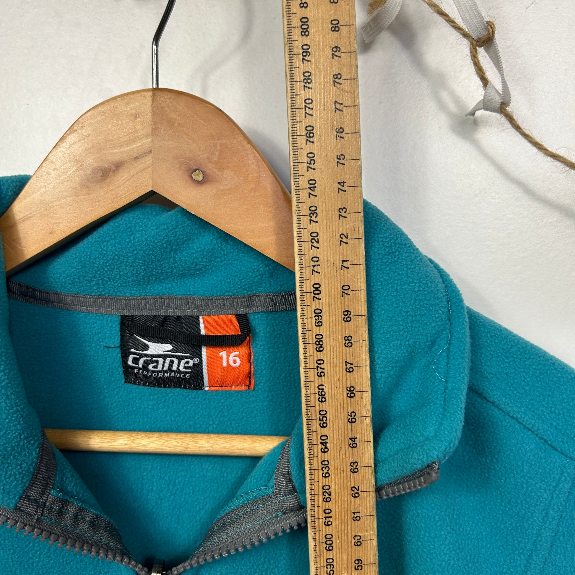 Teal fleece jacket front view on wooden hanger with measurement scale