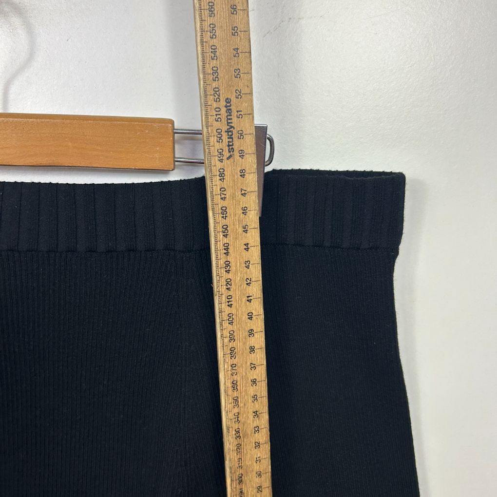 Black ribbed knit garment detail view with measuring tape