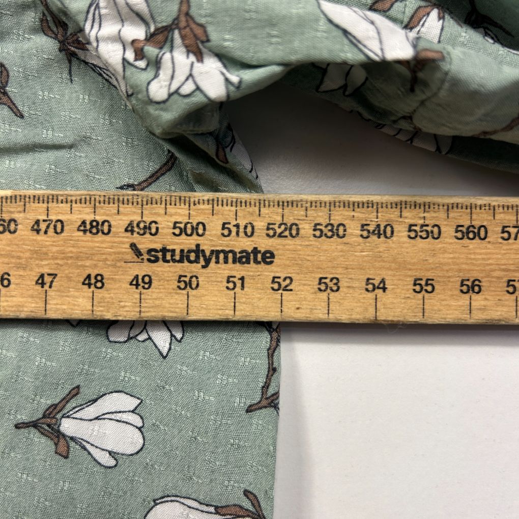 Green fabric with white floral print detail view with ruler
