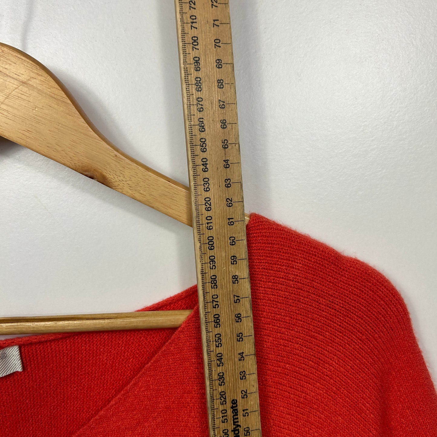 Red knit sweater detail view with wooden hanger and measuring tape