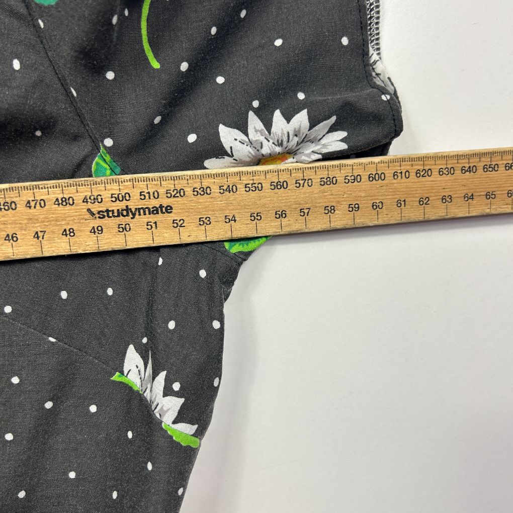Black fabric with white polka dots and white daisy floral print, detail view with measuring tape