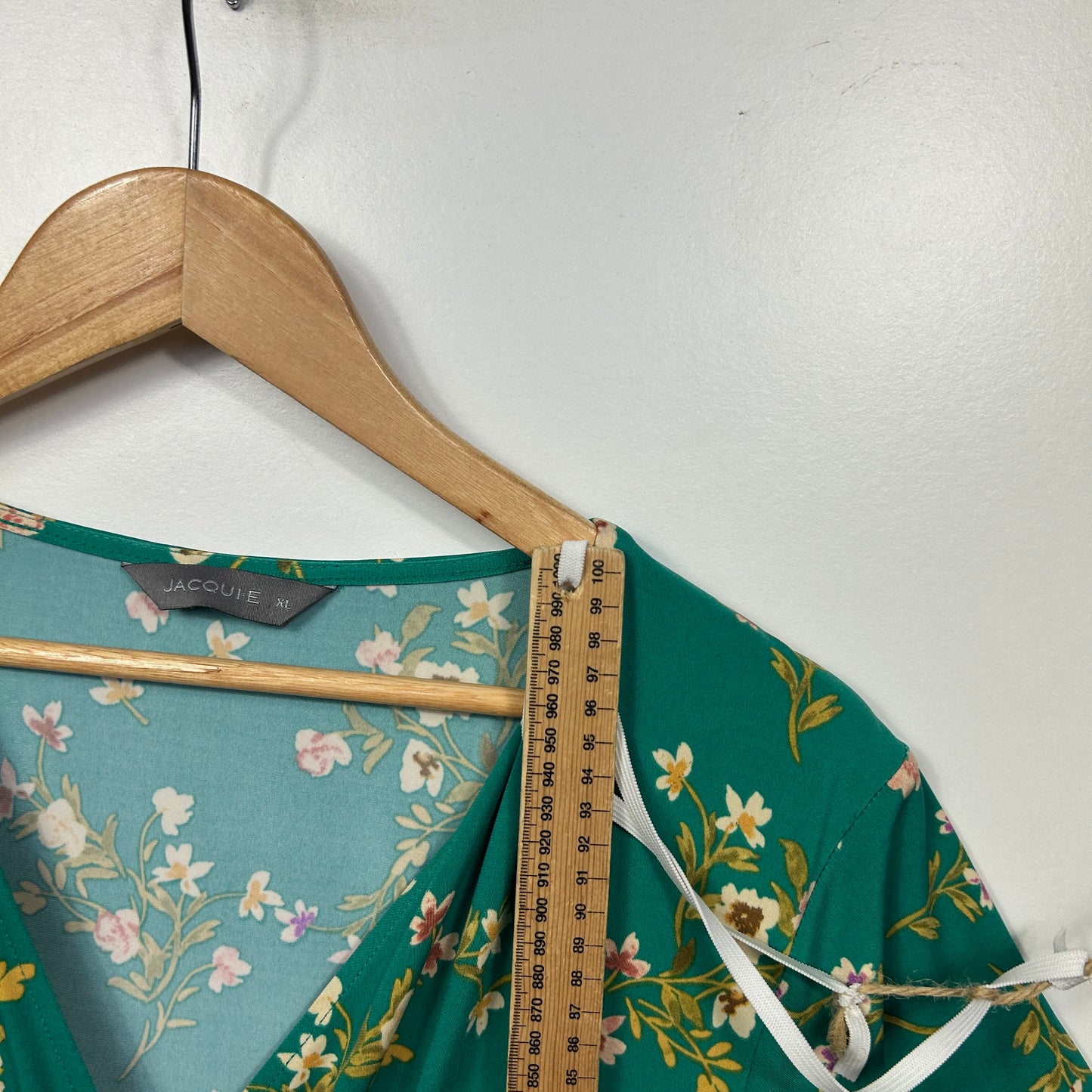 Green floral blouse detail view on hanger with measuring tape