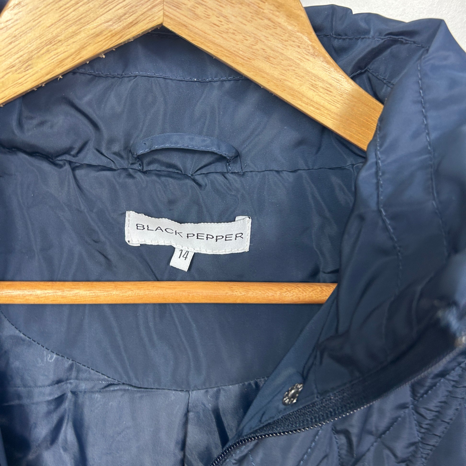 Navy puffer jacket detail view showing Black Pepper label on wooden hanger