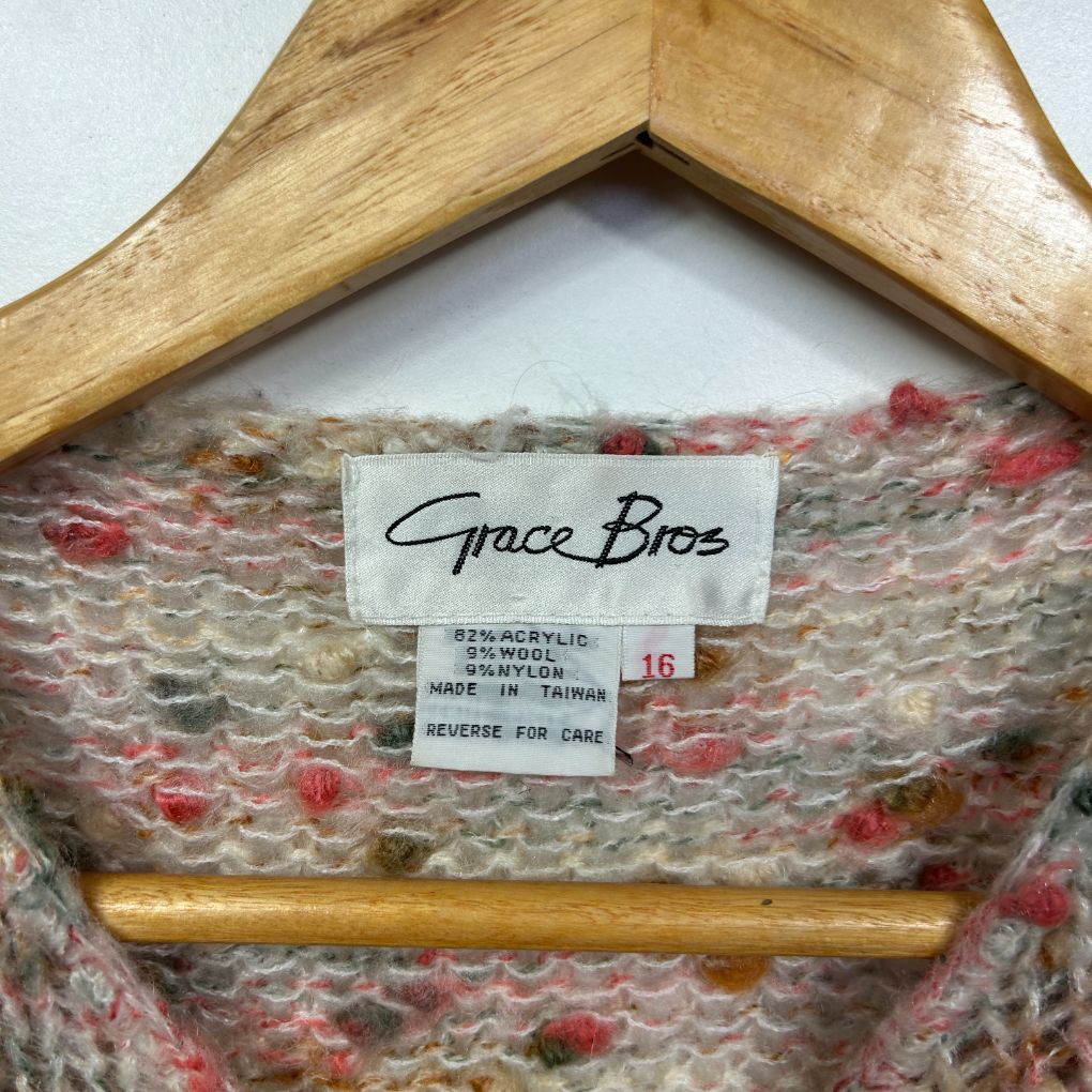 Beige knit sweater with red floral pattern on wooden hanger detail view