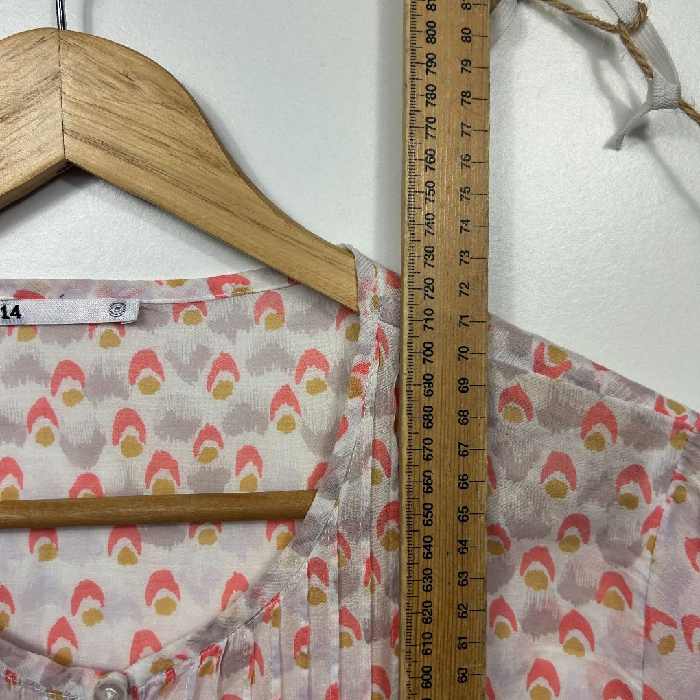 Pink and red floral patterned dress on wooden hanger detail view