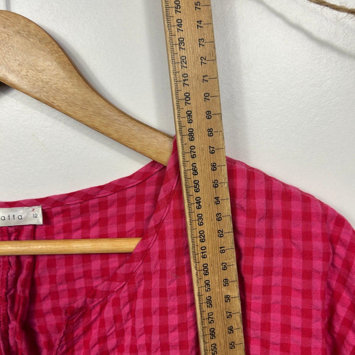 Pink checkered shirt front view on wooden hanger with measuring tape