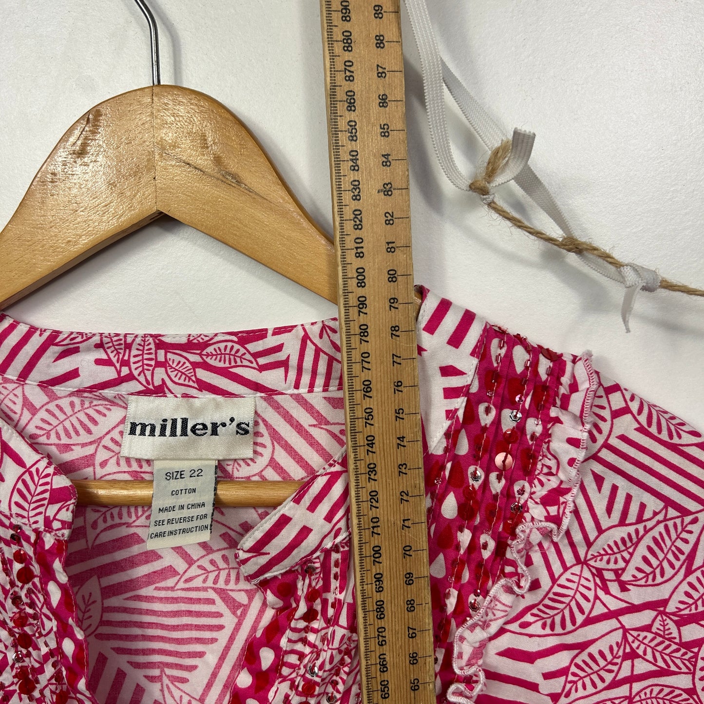 Pink and white patterned shirt detail view with wooden hanger and measuring tape