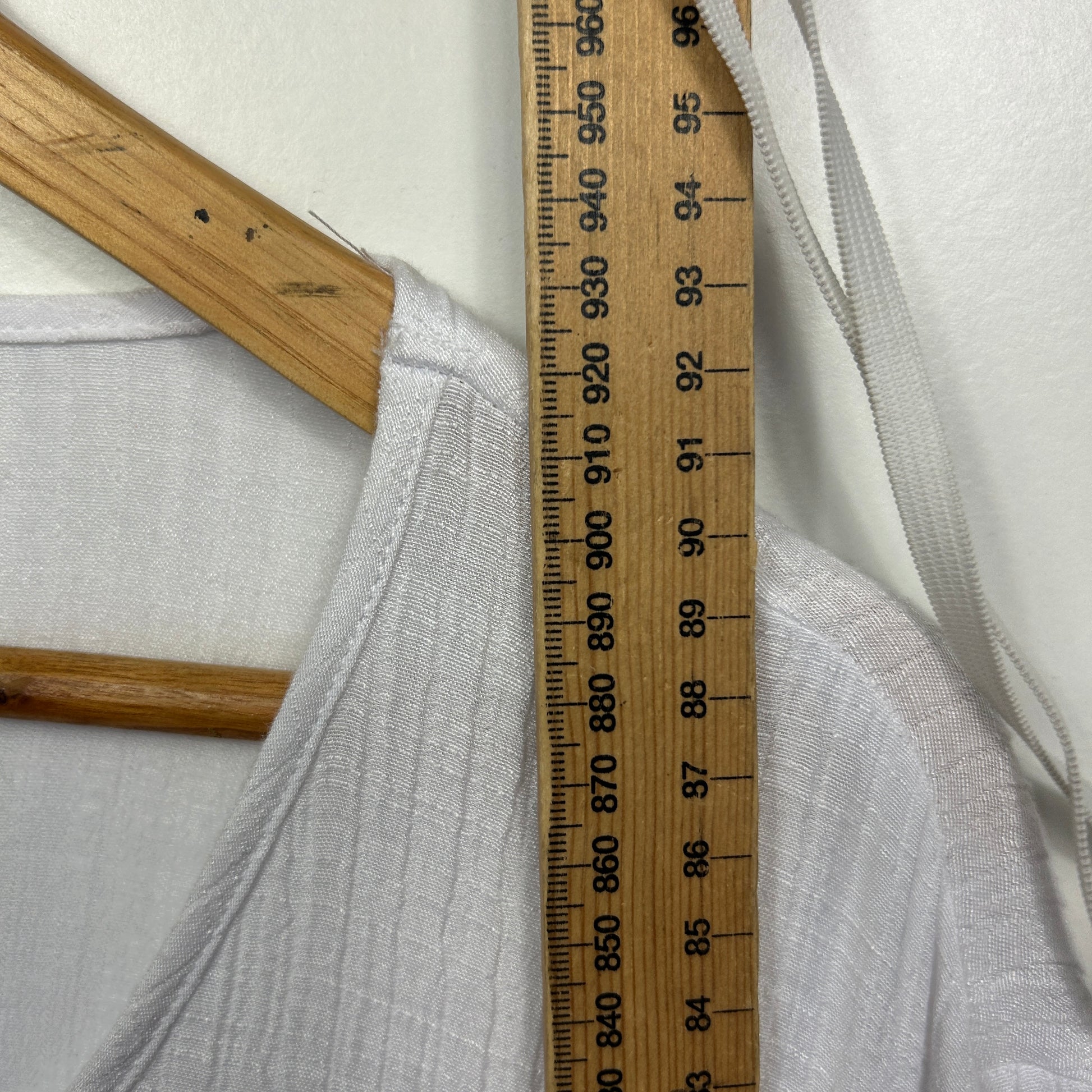 White ribbed fabric detail view with wooden hanger and measuring tape